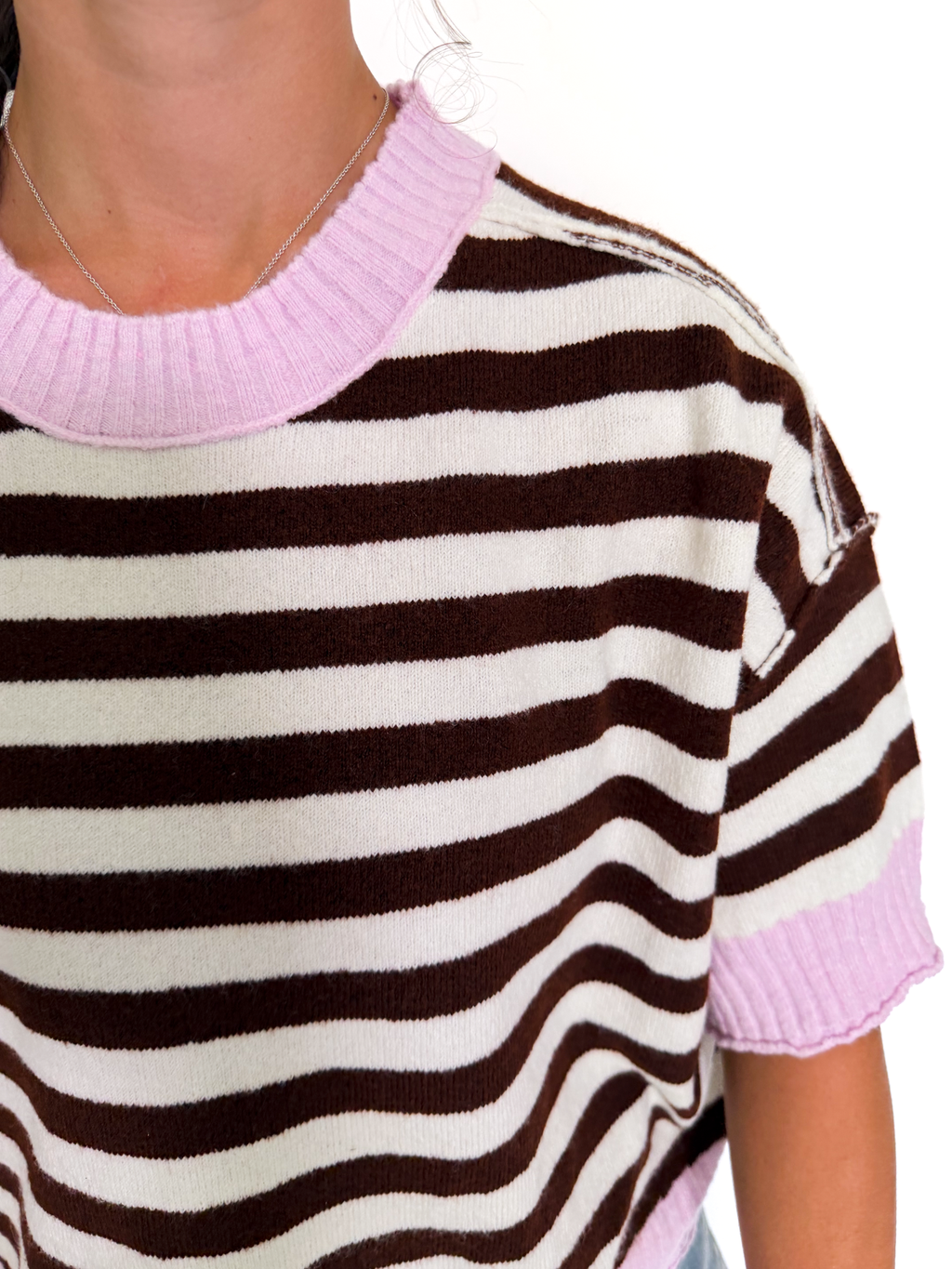 A close-up of a person wearing a short-sleeve knit top with horizontal brown and off-white stripes and light pink ribbed trim at the crew neck and sleeve cuffs.