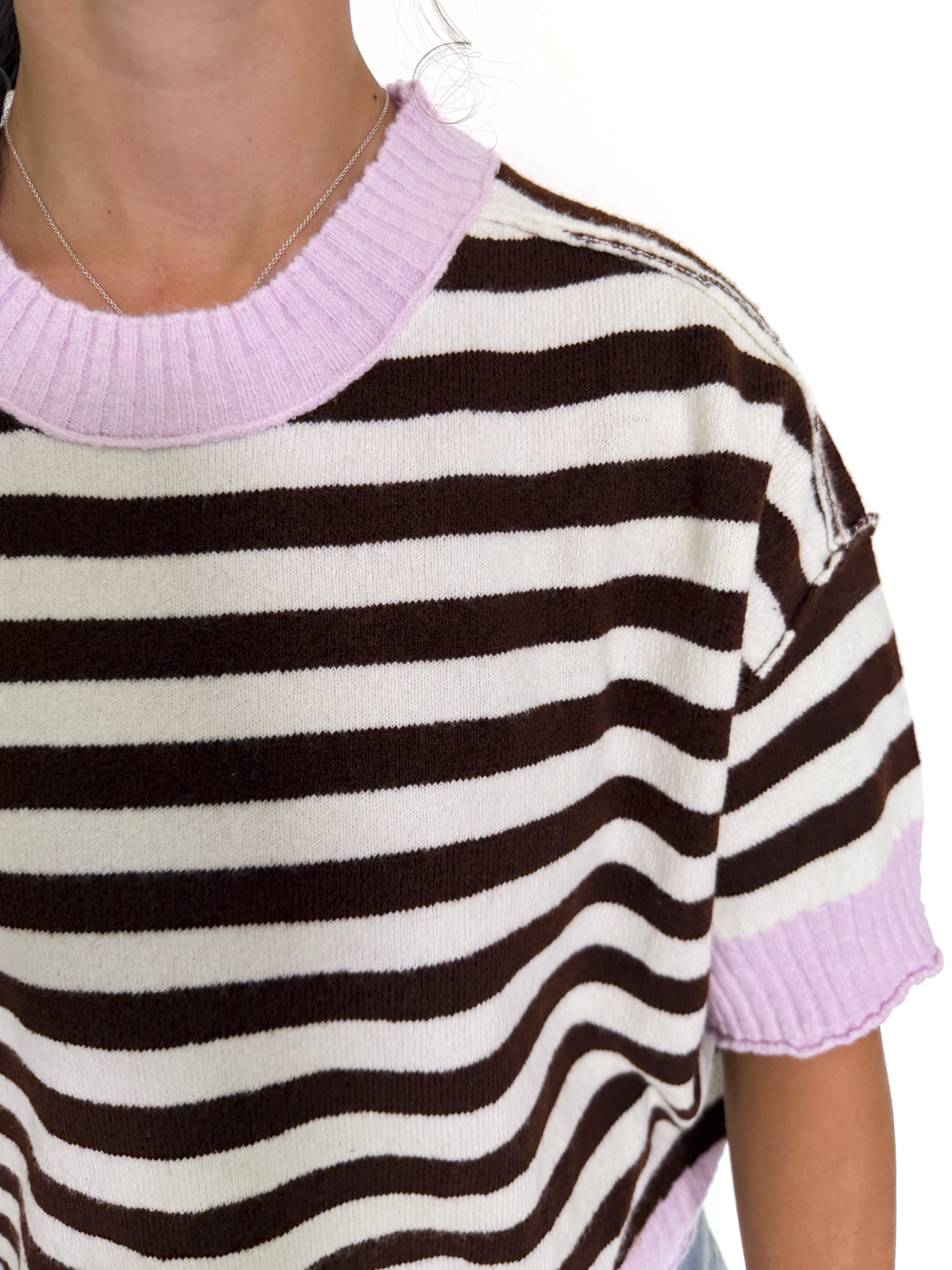 A close-up of a person wearing a short-sleeve knit top with horizontal brown and off-white stripes and light pink ribbed trim at the crew neck and sleeve cuffs.