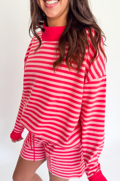 A woman wearing a matching red and white striped lounge set, featuring a long-sleeve top and shorts, against a plain white background.