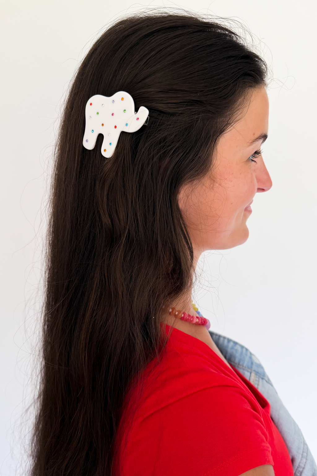 A woman in profile wearing a white elephant-shaped hair clip decorated with small red and green dots, shown against a plain white background.