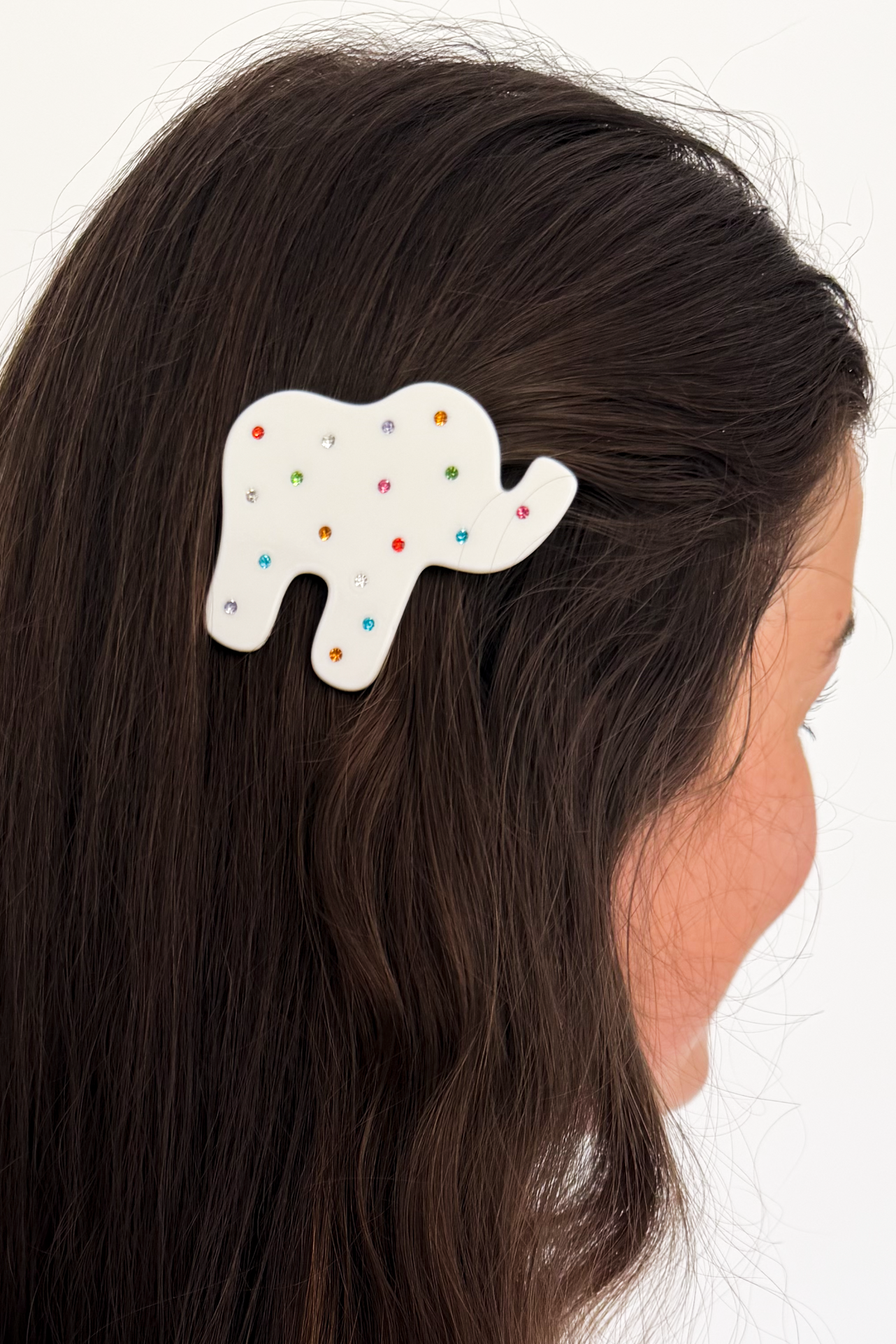 A white elephant-shaped hair clip decorated with small multicolored polka dots, shown clipped to the side of a woman's dark brown hair against a plain white background.