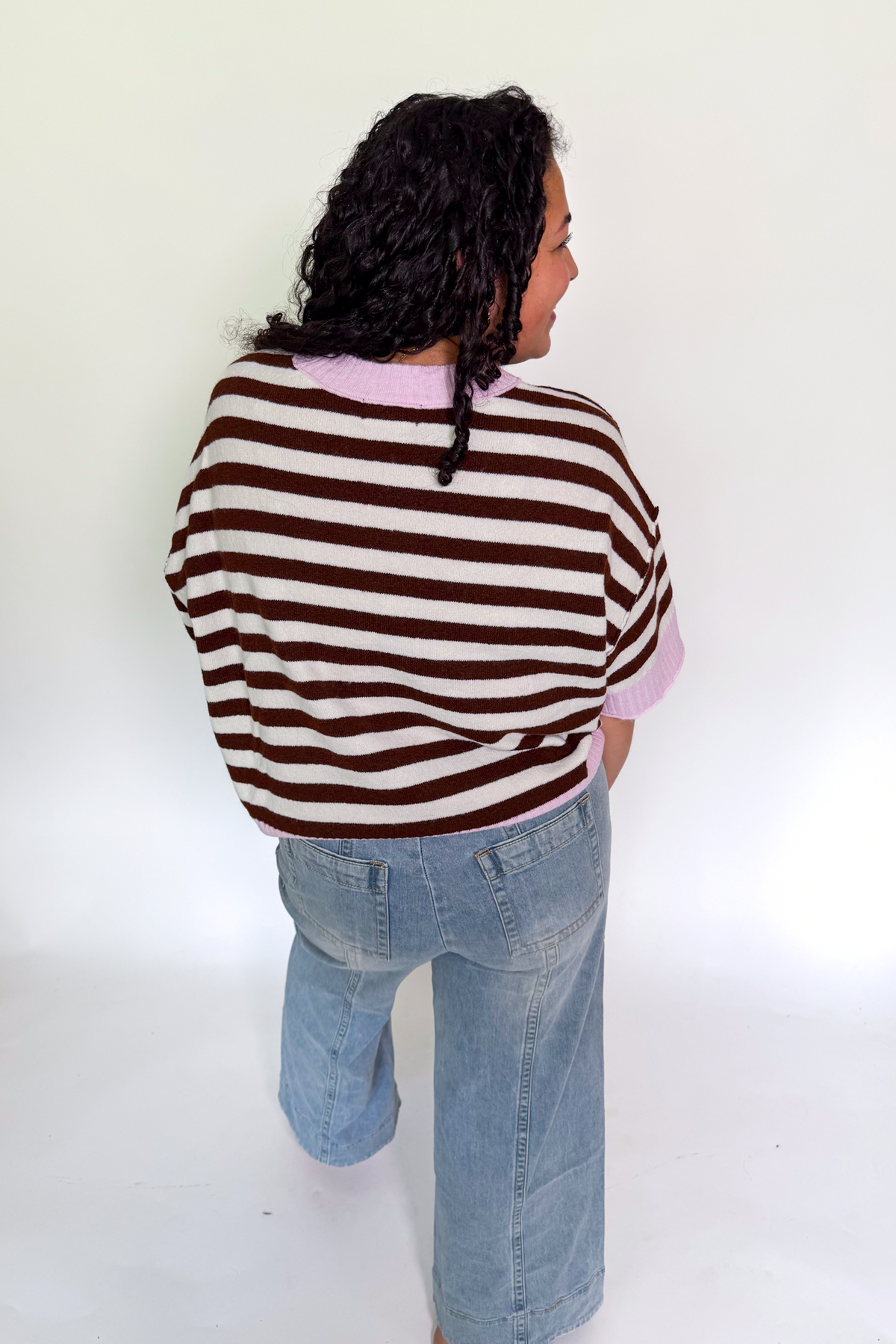 A person shown from the back wearing a brown and cream striped knit sweater with light pink inner collar and cuffs, paired with light blue jeans, against a plain white studio background.