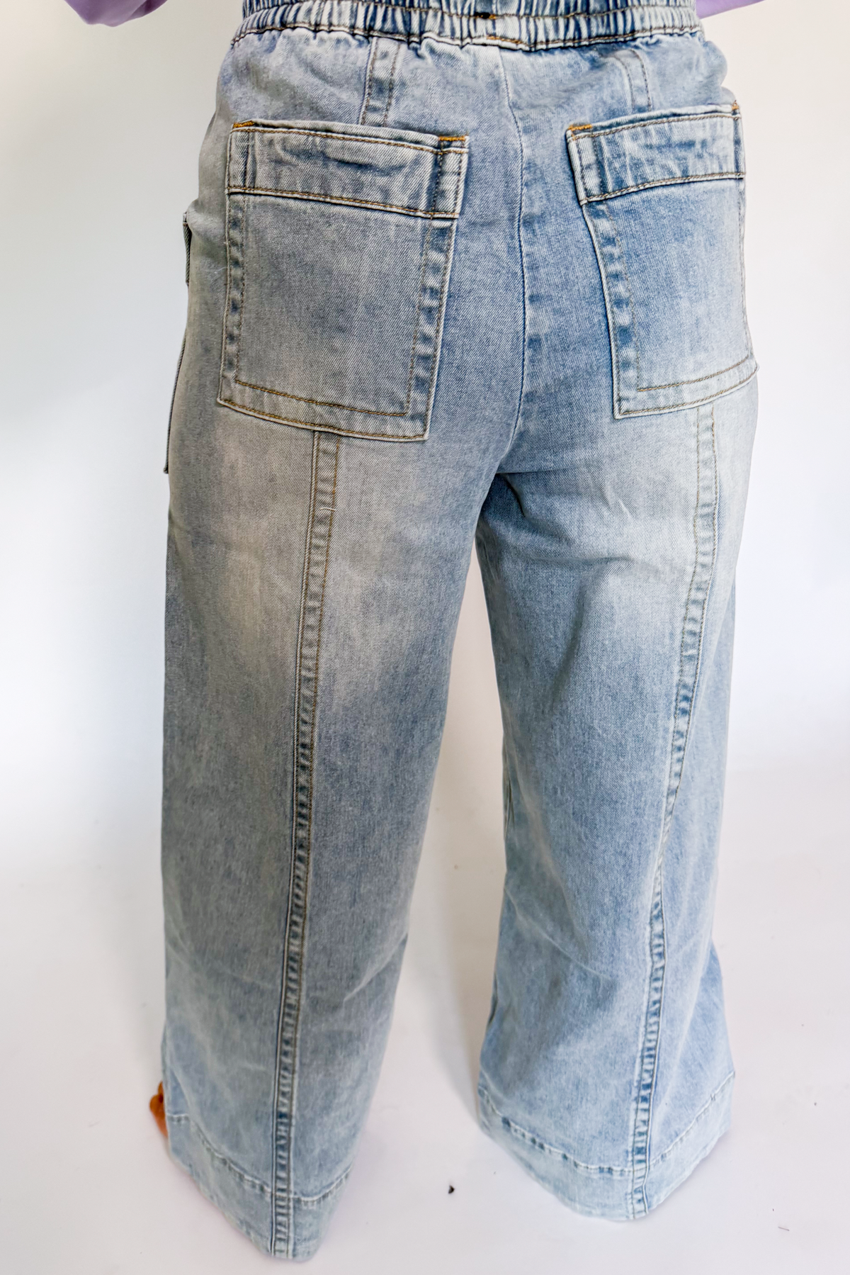 Light blue wide-leg denim jeans shown from the back, featuring a button fly, two large patch back pockets, and contrast stitching, photographed against a white studio background.