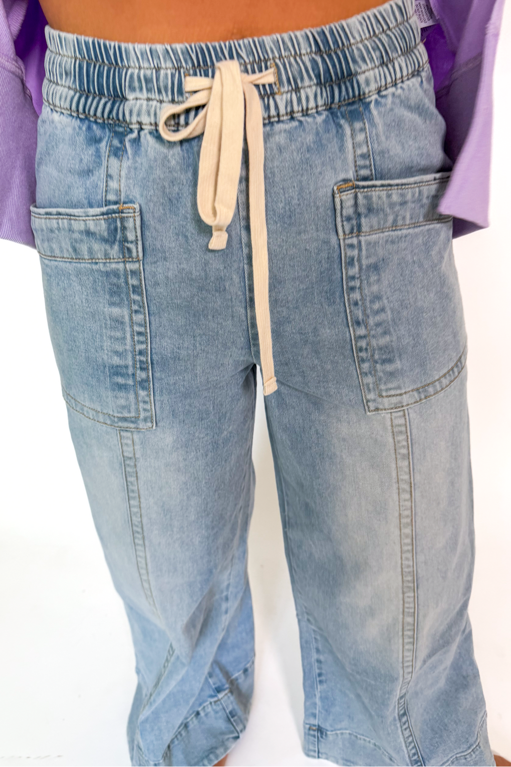 A person wearing light-wash blue denim drawstring pants with side pockets and a relaxed straight-leg fit, shown from the waist down against a plain white background.