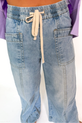 A person wearing light-wash blue denim drawstring pants with side pockets and a relaxed straight-leg fit, shown from the waist down against a plain white background.