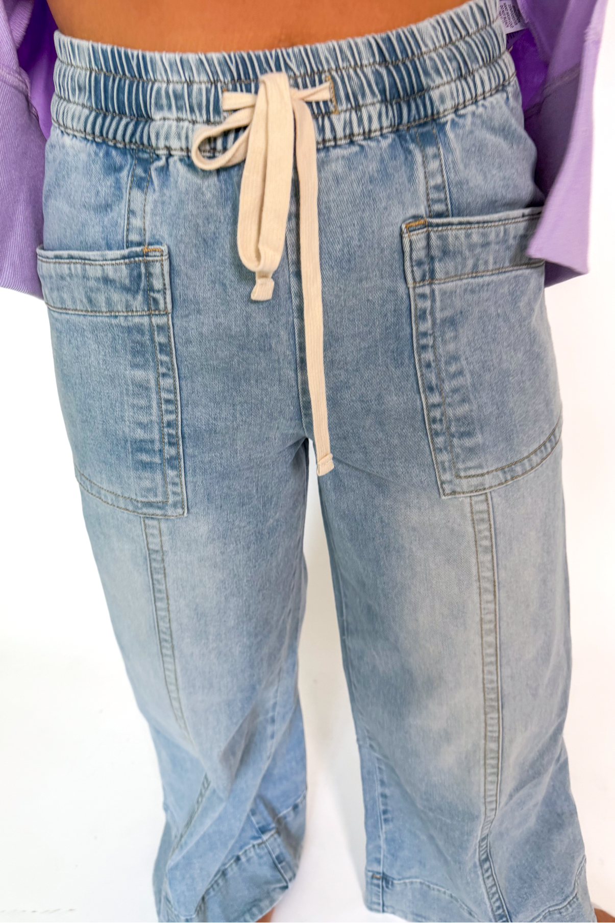 A person wearing light-wash blue denim drawstring pants with side pockets and a relaxed straight-leg fit, shown from the waist down against a plain white background.