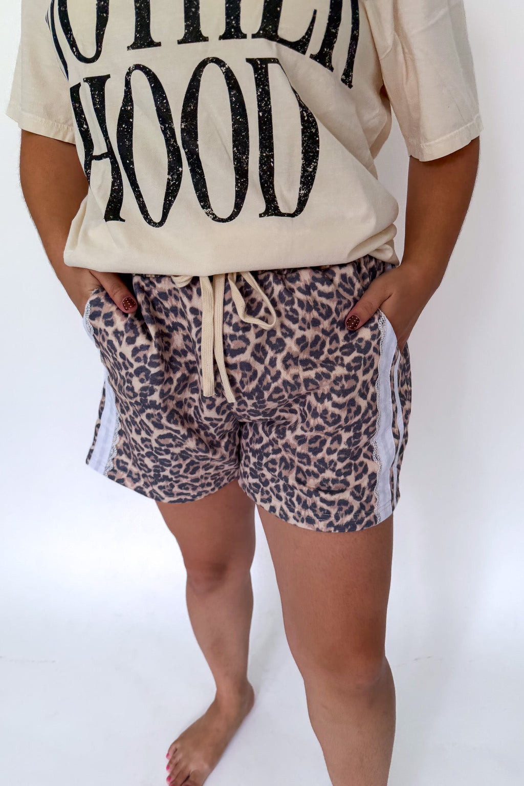 A person wearing leopard-print shorts with white side panels and a cream drawstring, paired with a cream graphic t-shirt, shown against a plain white studio background.