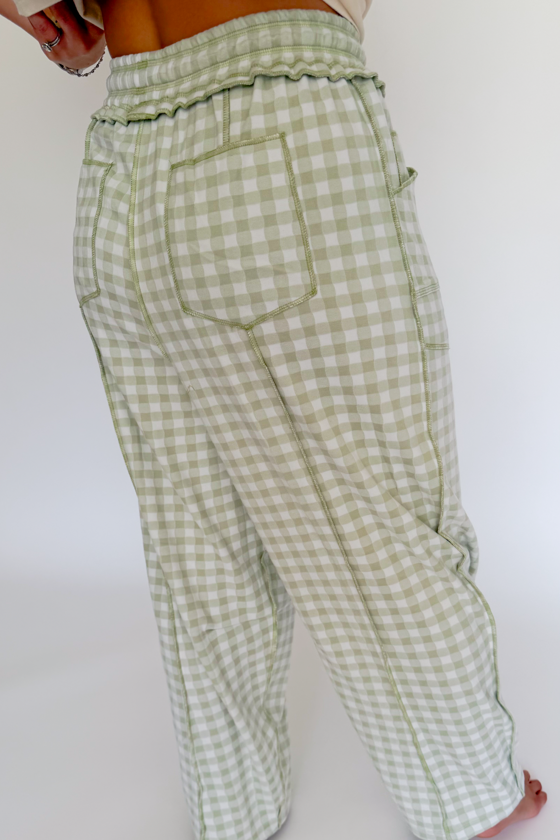 A person wearing light sage green and white gingham pants, shown from the back against a plain white background.